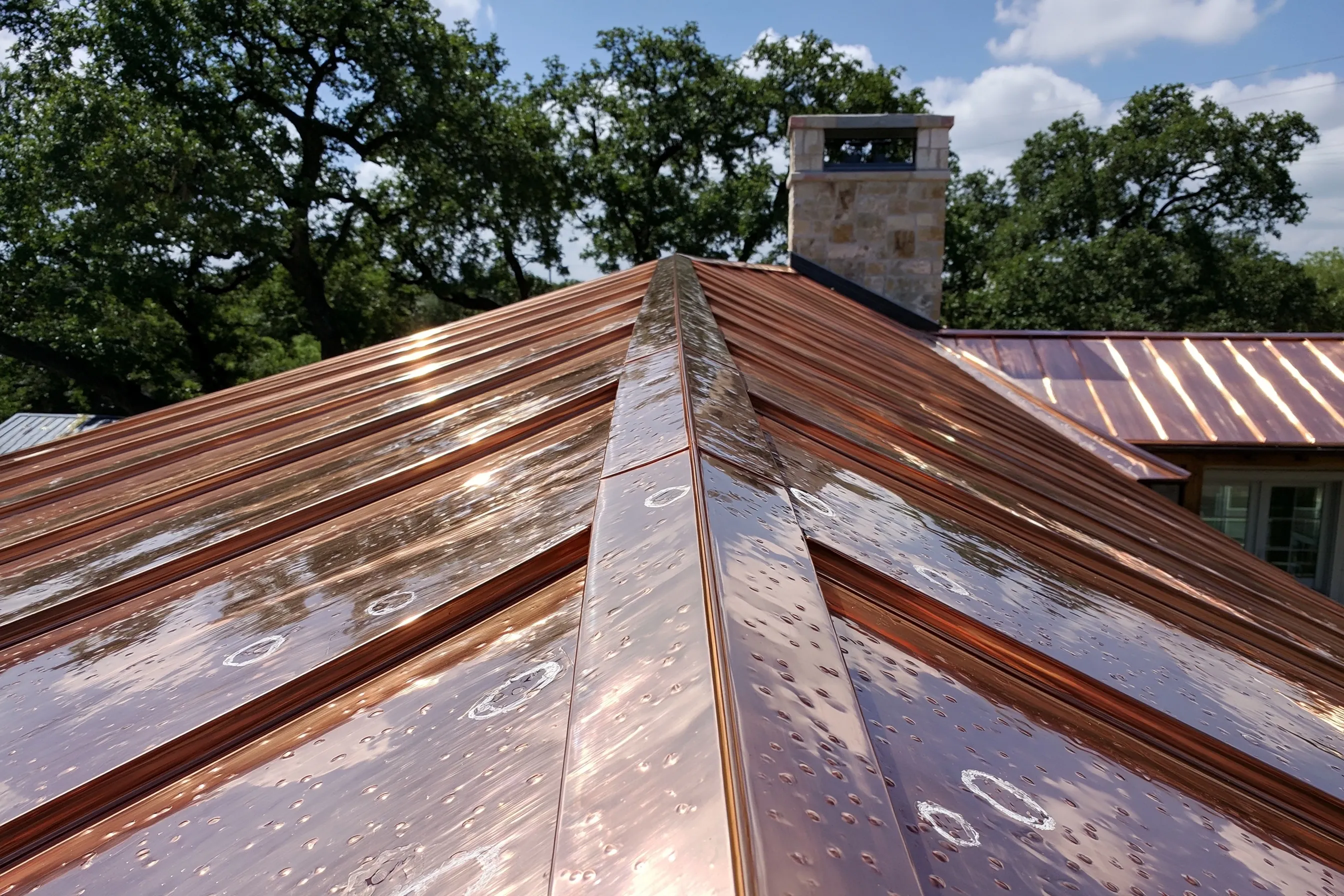 Copper standing-seam roof panels with small hail dents on a house roof